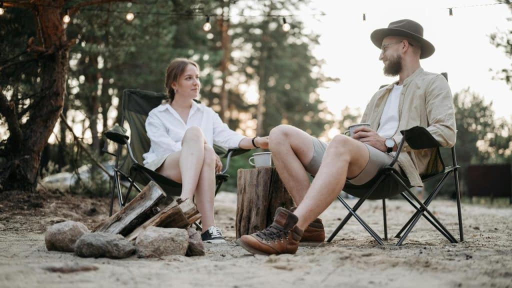 A man and woman sitting by a campfire and talking outdoors.