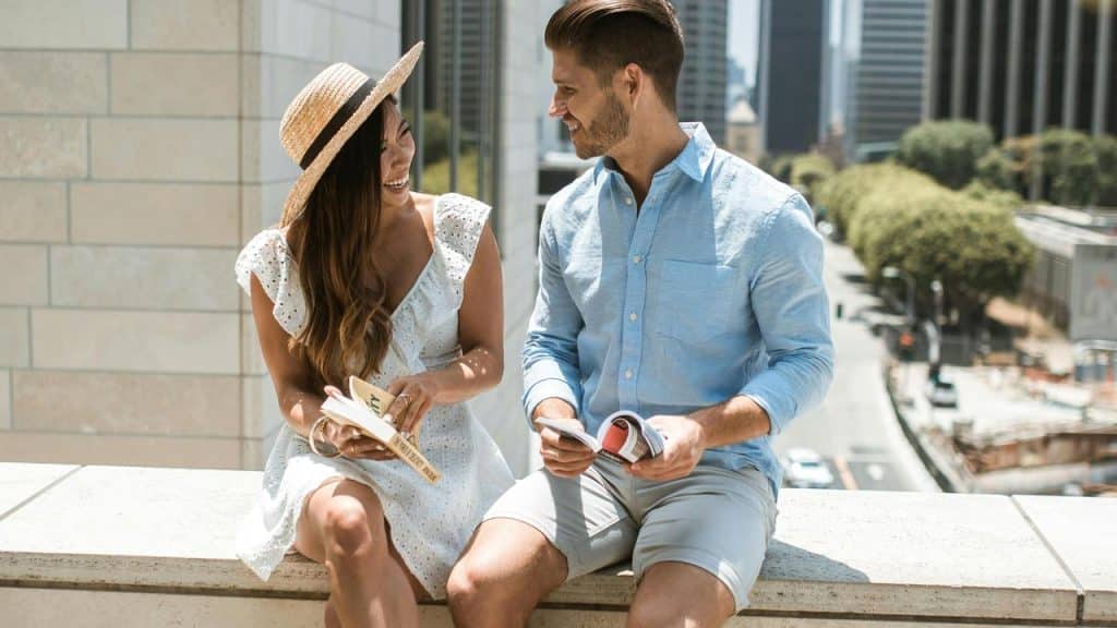 A couple sitting outdoors on a ledge, smiling and reading together in the city.