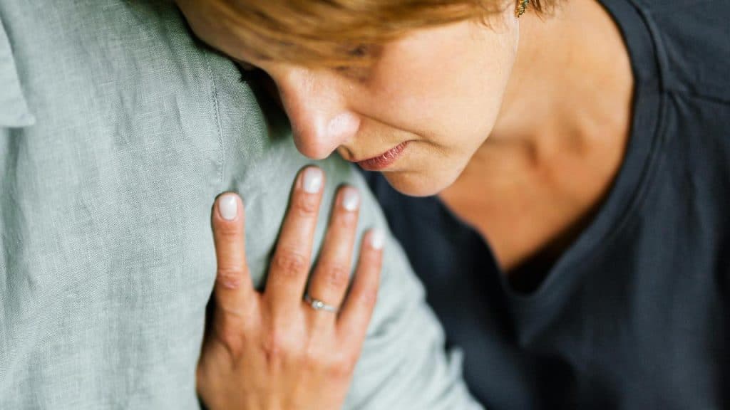A woman resting her head on someone’s shoulder with her hand placed gently on them.