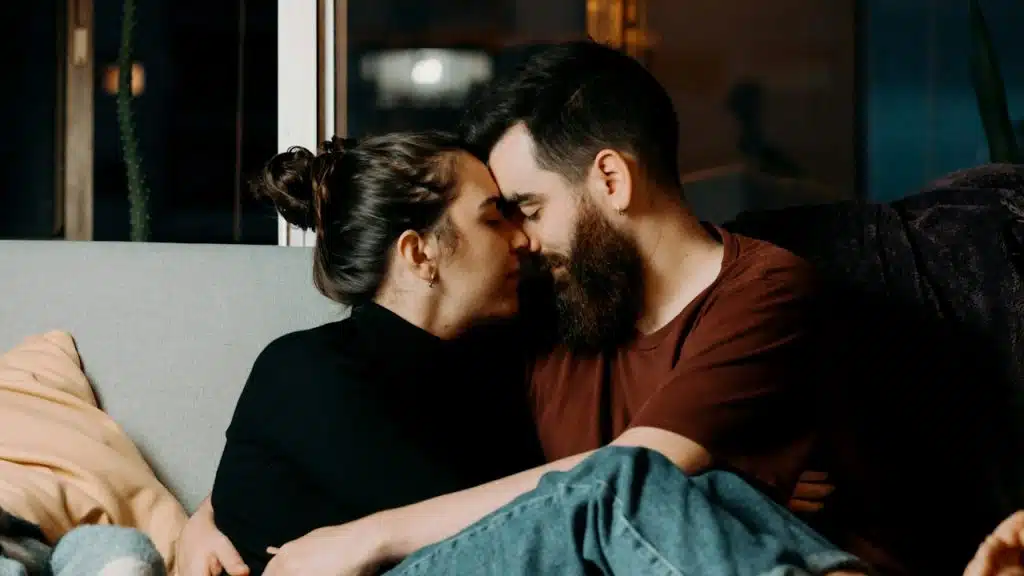 A man and a woman touching their foreheads while sitting on a couch.