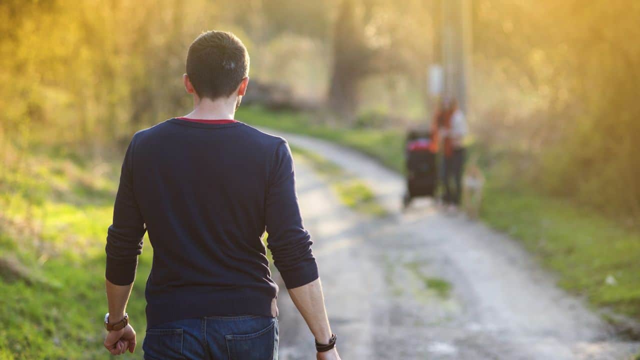 A man walks away on a dirt path with blurred figures in the distance.