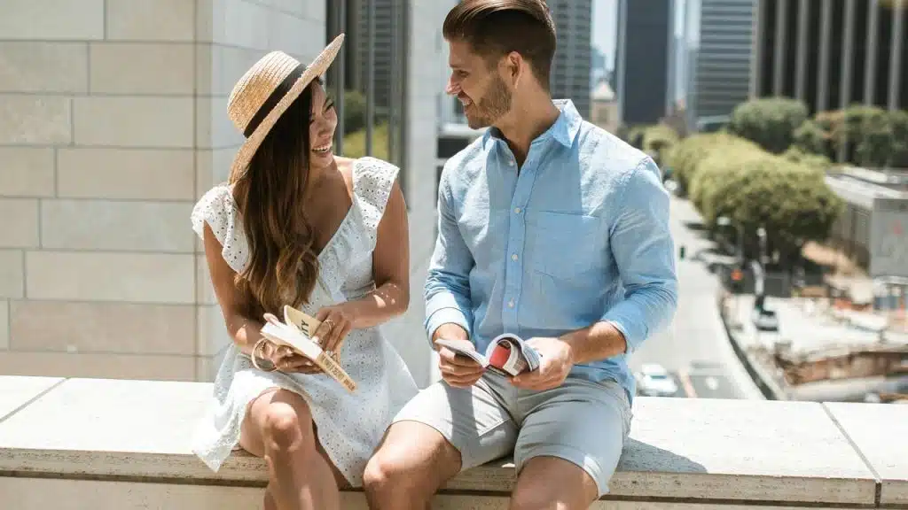 A couple sitting outdoors on a ledge, smiling and reading together in the city.