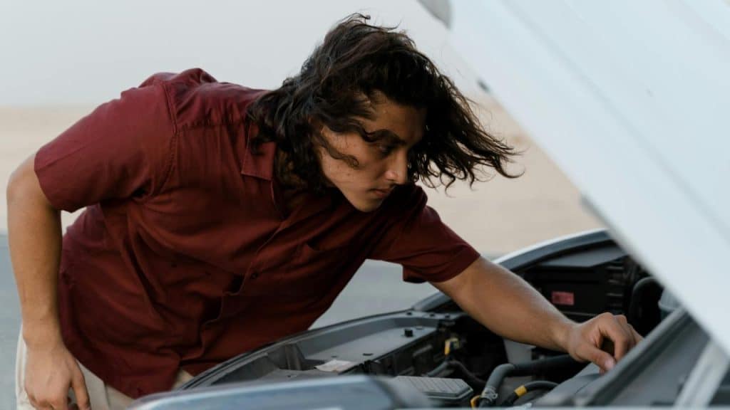 A person inspecting the engine of a car with the hood open.