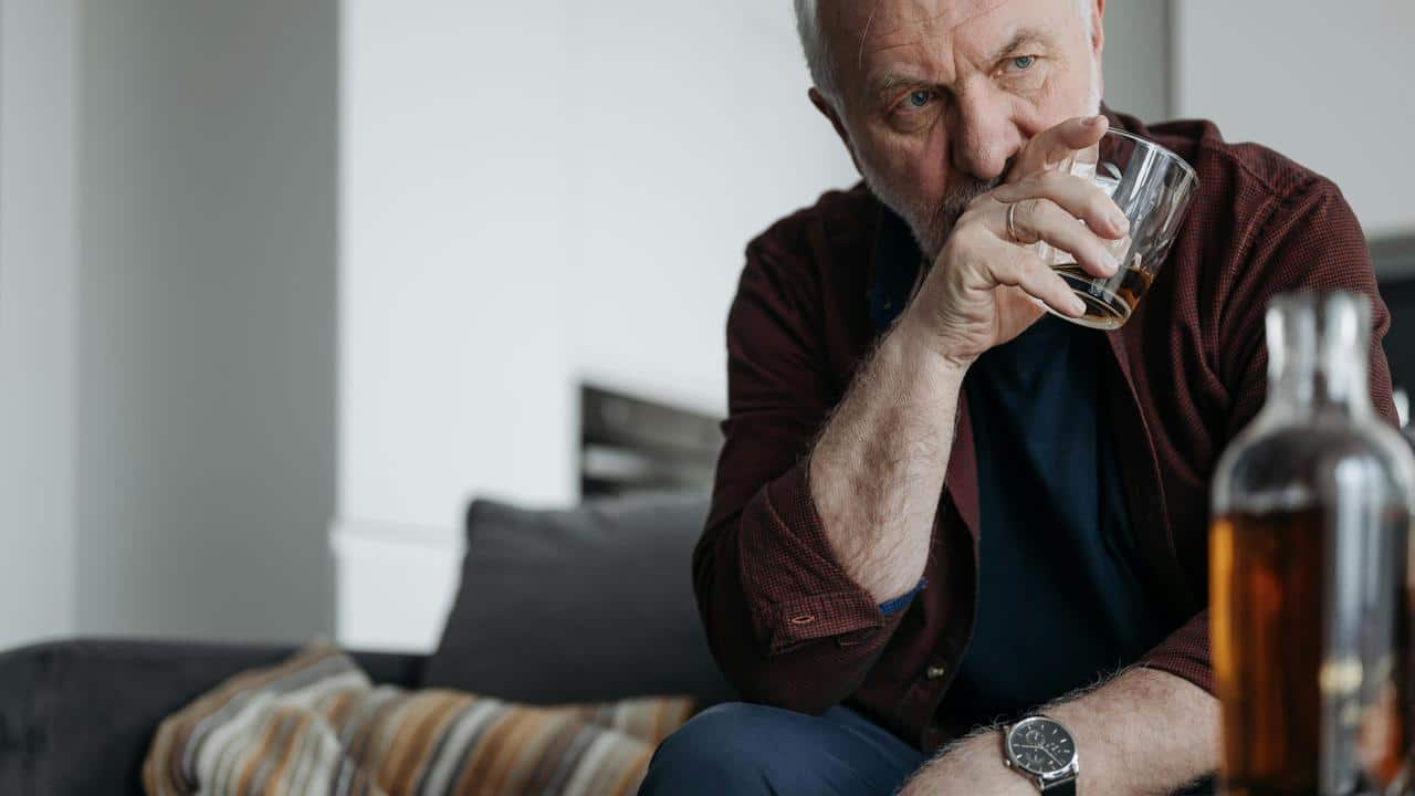 A man sitting on a couch drinking from a glass of liquor.