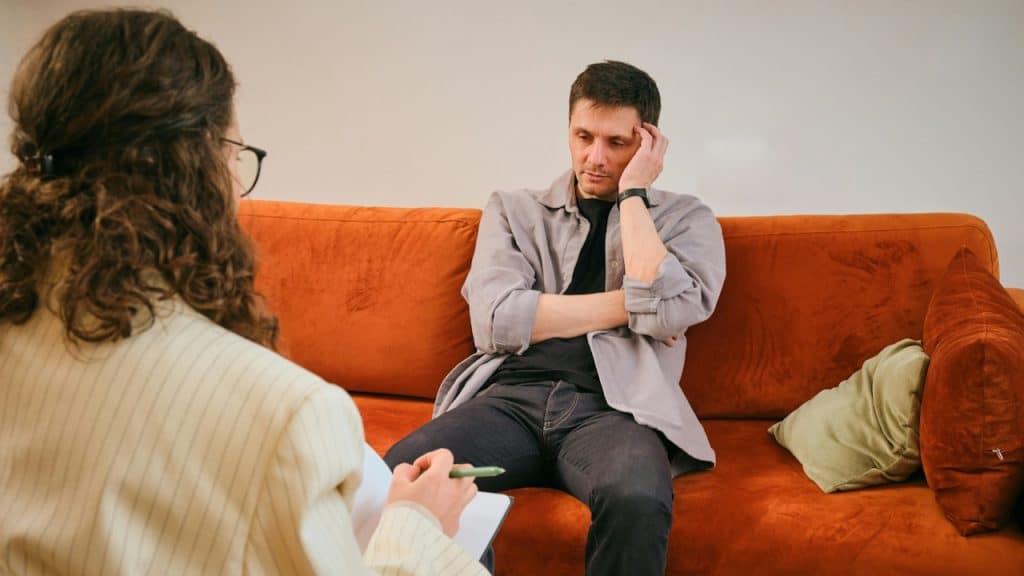 A man sitting on a couch is talking to a therapist in a session.