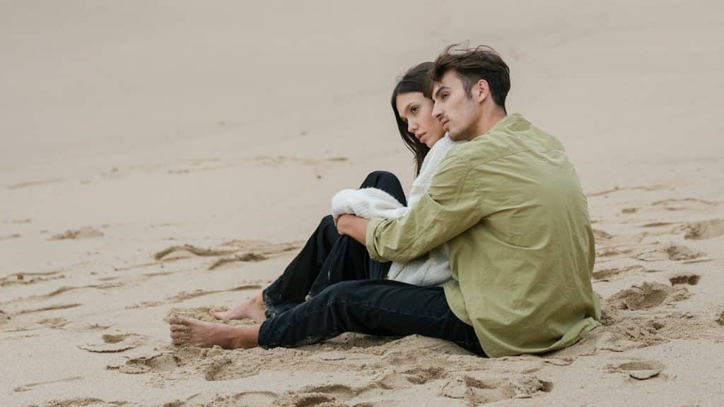 A couple is sitting close together on a sandy beach