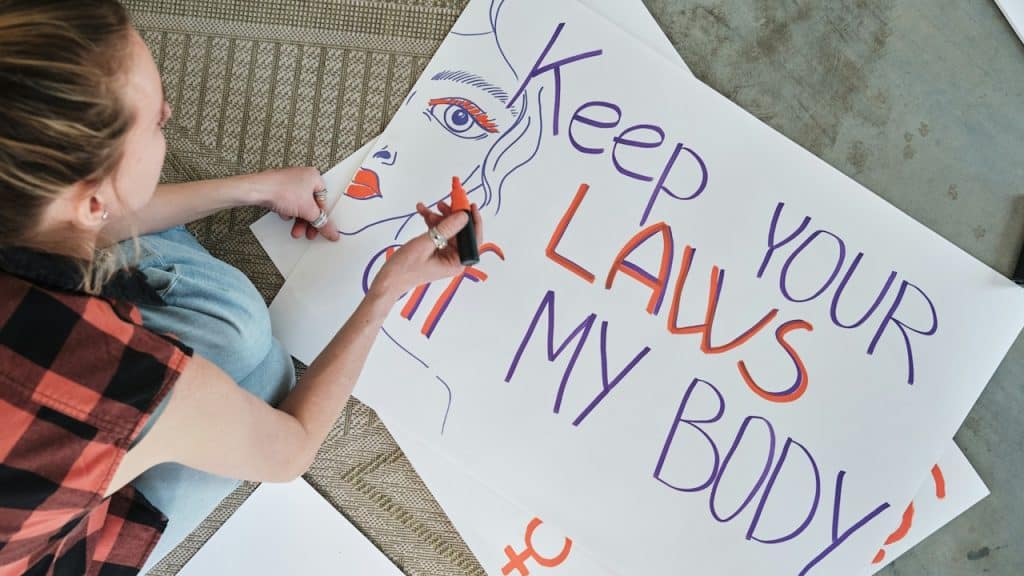 A woman is writing on a sign that says, "Keep your laws out of my body."