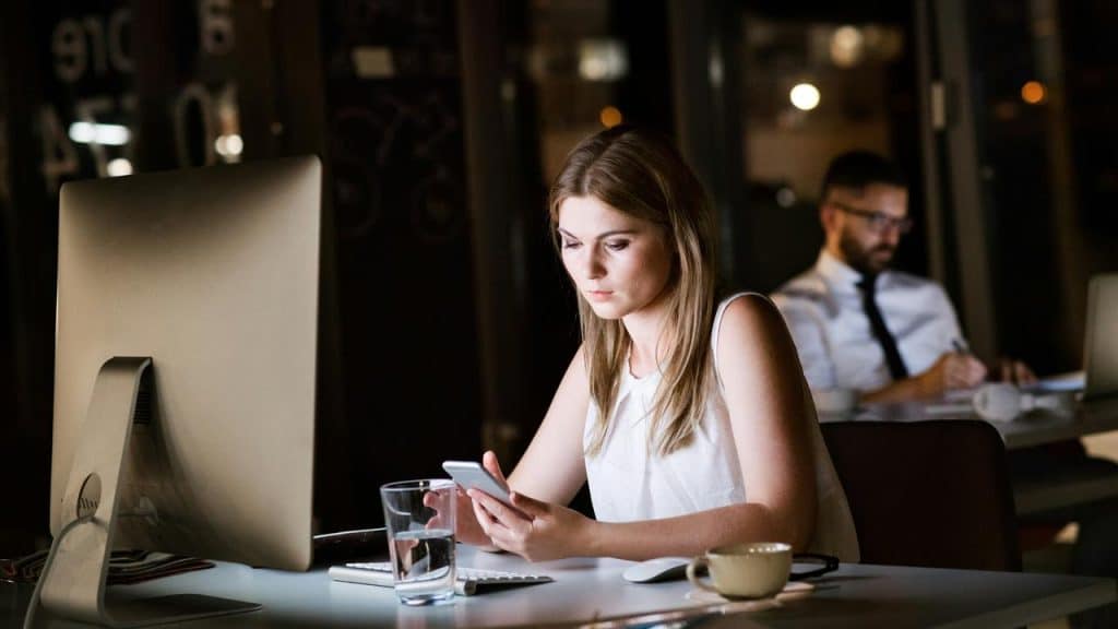 A woman working late in an office looking at her smartphone.