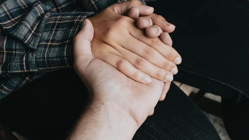 A close-up of two people holding hands in a comforting gesture.