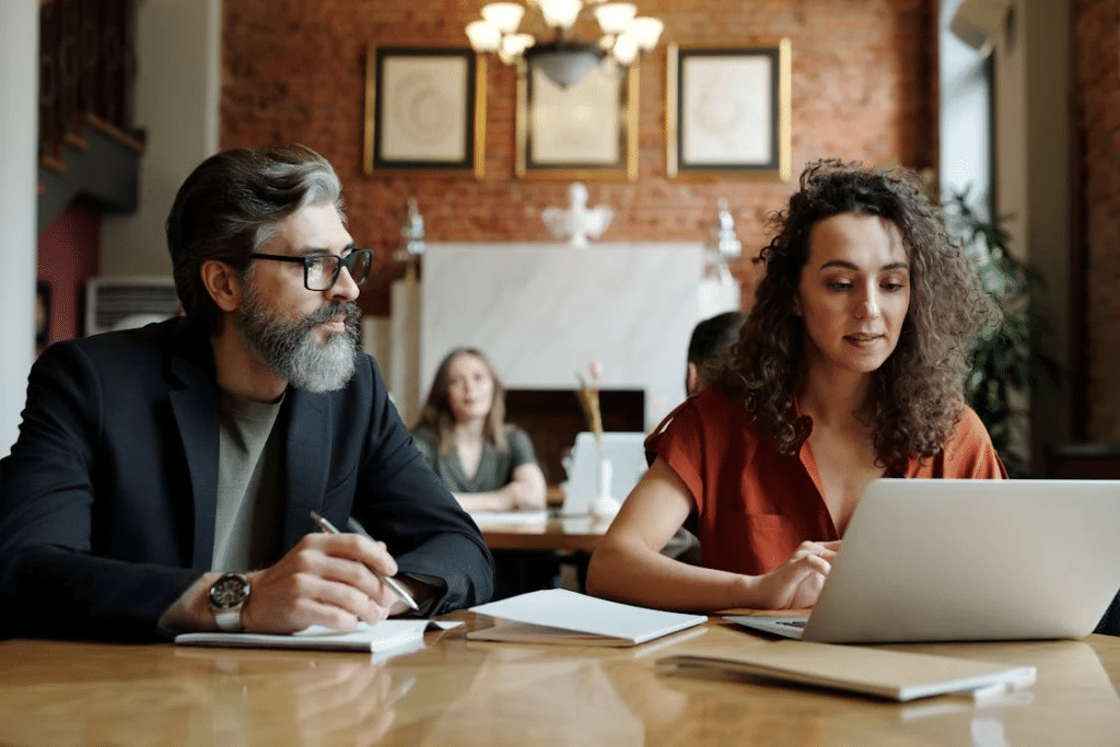 Man Taking Notes and Woman Scrolling on a Laptop