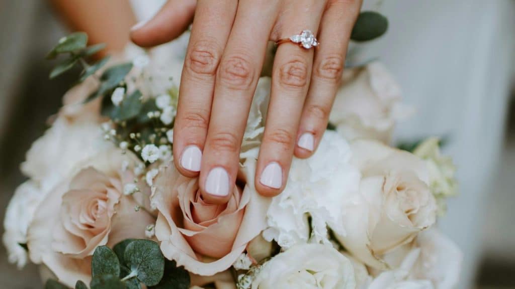 A close-up of a hand with an engagement ring resting on a bouquet of roses.