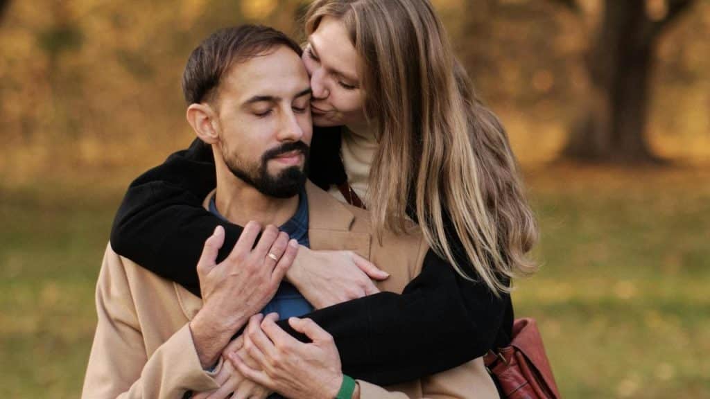 A woman hugging and kissing a man on the cheek outdoors.