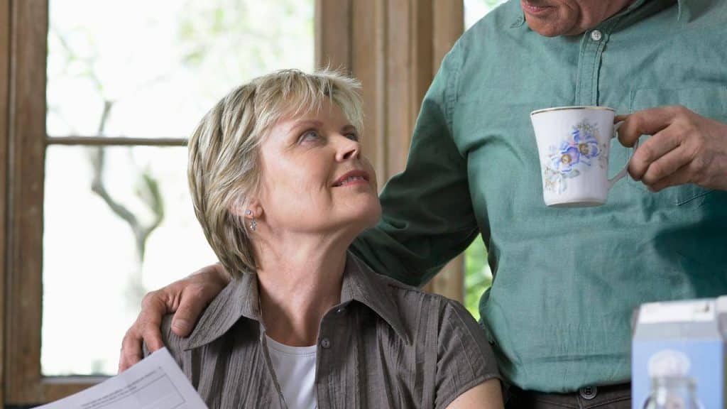 A woman looks up at a man holding a mug with his hand on her shoulder.