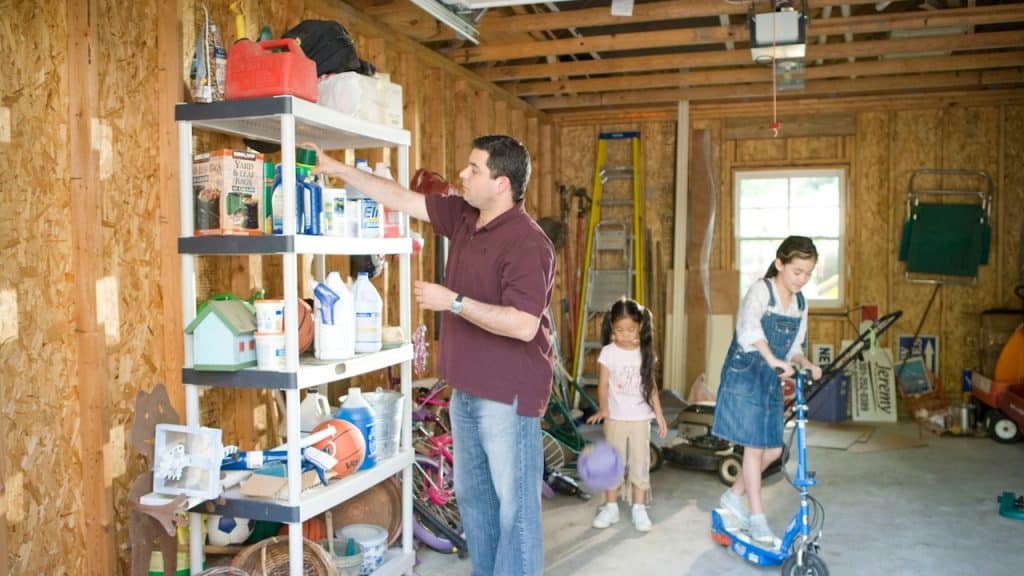 A man cleaning a cupboard while his daughters are playing near him.