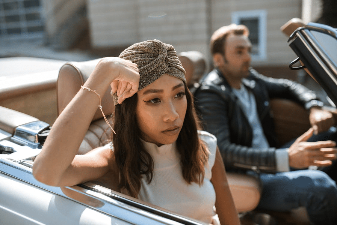 Woman in white tank top sitting in a car feeling annoyed