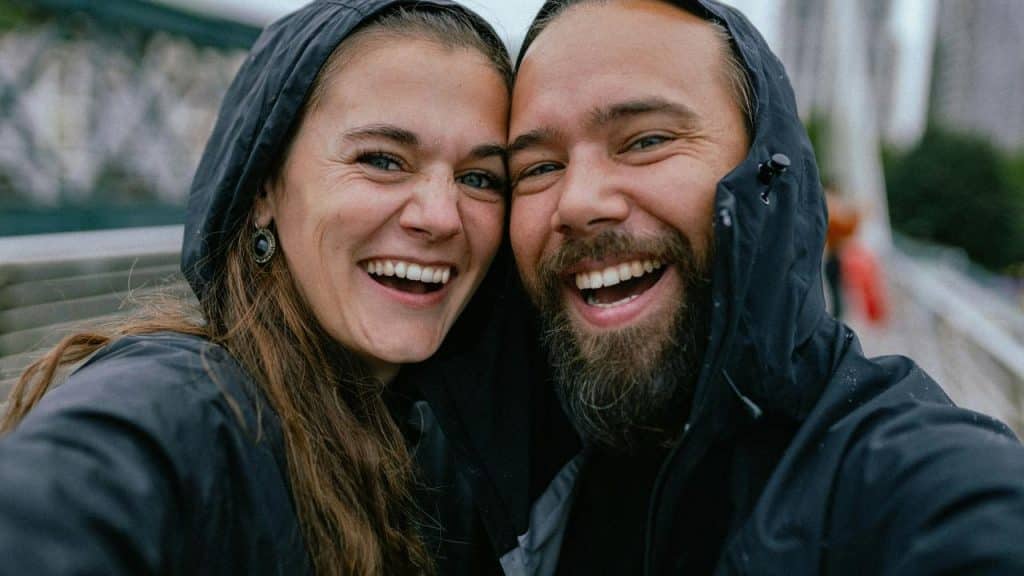 A couple takes a cheerful selfie together outdoors in rainy weather.