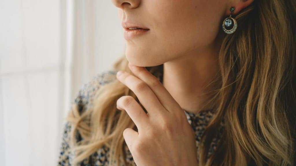 A close-up of a person touching their chin, wearing earrings and a patterned top.