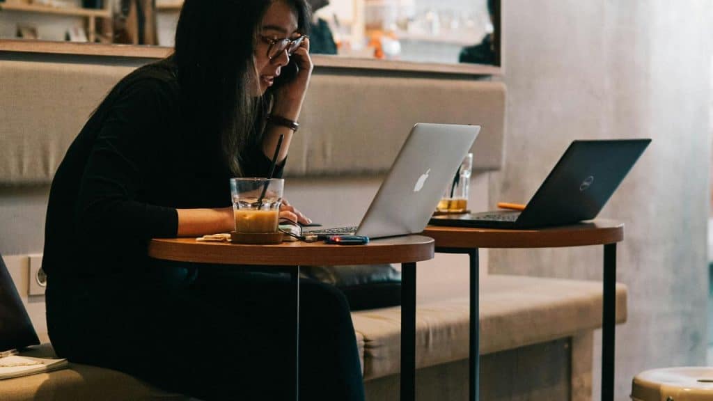 A woman working on a laptop in a cafe while talking on the phone.