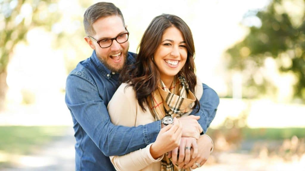 A couple hugging each other and smiling outdoors.