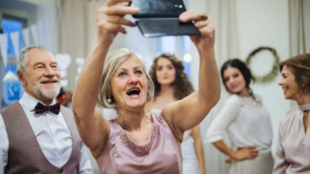 An elderly woman on a wedding party taking a selfie with her husband and other woman.
