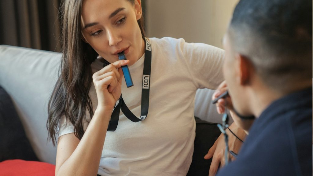 A woman sitting on a couch holding a vape in her mouth.