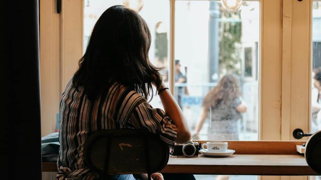 A woman sitting by a window with coffee and a camera.