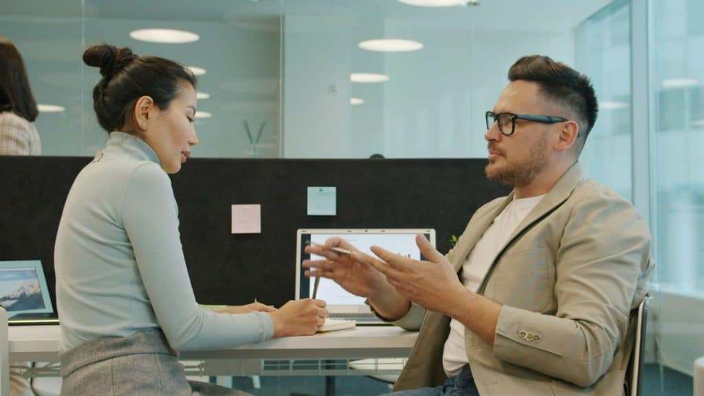 Two people, a woman and a man, are sitting at a desk and discussing something in an office.