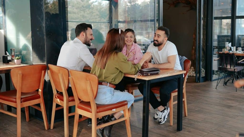 Four people sitting at a wooden table in a café or restaurant, smiling and talking.