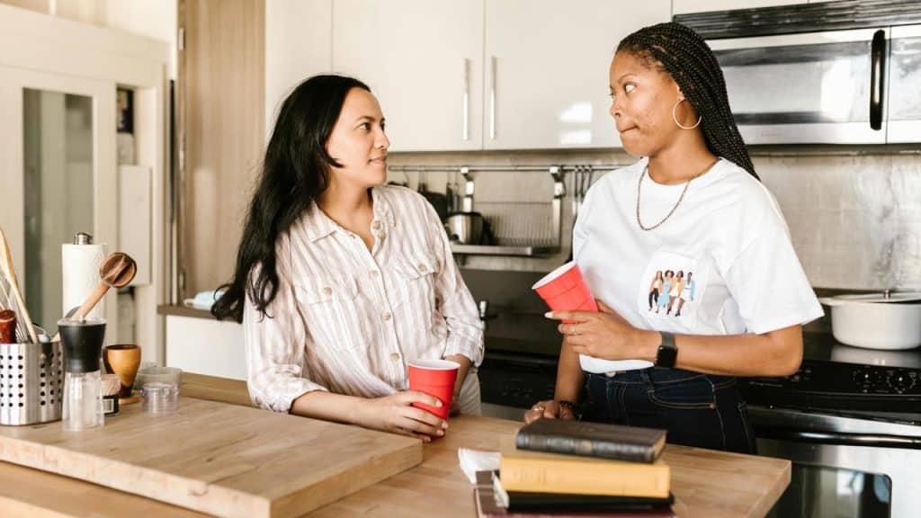 A pair of women having a conversation in a kitchen while holding red cups.