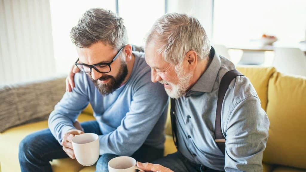 Two men of different generations sitting together on a couch, holding mugs.
