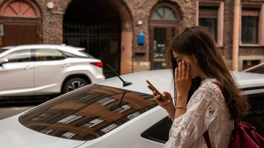 A woman wearing a white blouse using phone standing beside a white vehicle.
