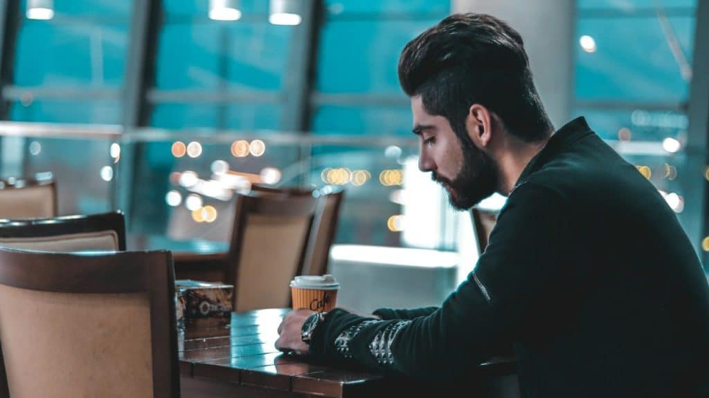 Young man with a beard sitting at a dark wooden table with a coffee cup.