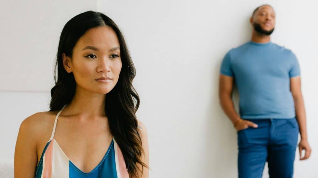 A focused portrait of a woman looking away, with a man standing in the background.