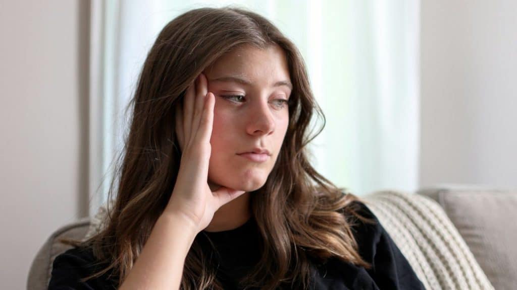 Young woman with brown hair resting her head on her hand and looking away indoors.