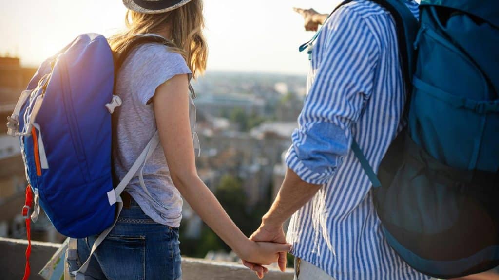 A couple with backpacks holds hands while sightseeing outdoors.