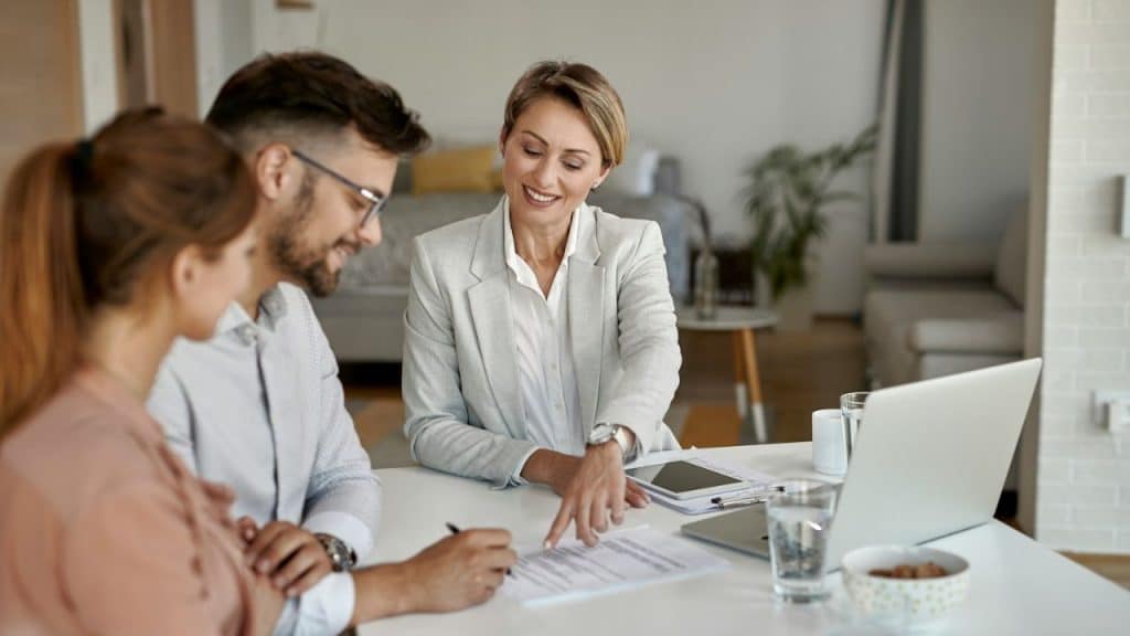 Woman advising a smiling couple sitting at a table with documents and a laptop.