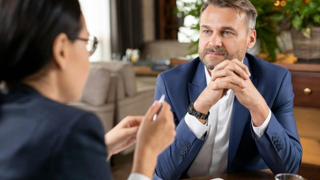 A man in a blue suit attentively listening during a conversation at a table.