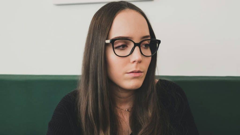 A young woman with long dark hair and black-framed glasses looks off-camera.