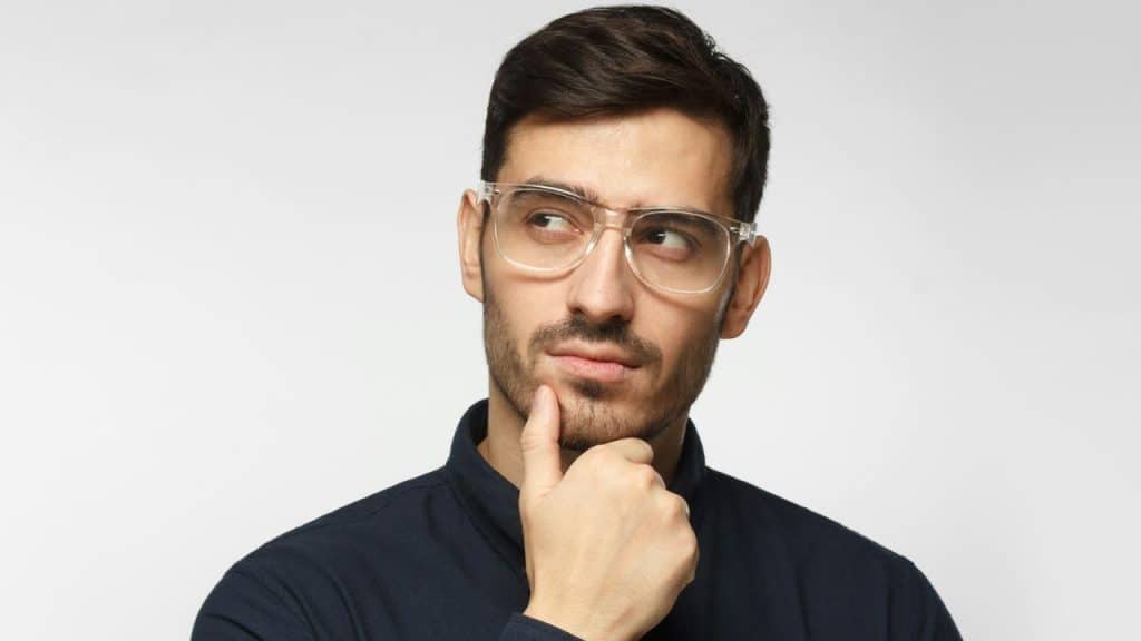 Man in glasses and a dark shirt, hand on his chin, looking away thoughtfully.