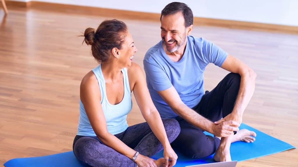 A Man and a woman sitting on a blue yoga mat.