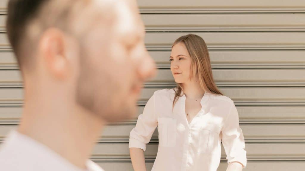 A woman looking to the side and wondering while a man stands in the foreground.