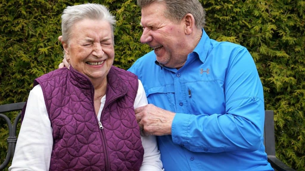 An elderly couple sitting outdoors laughing together.