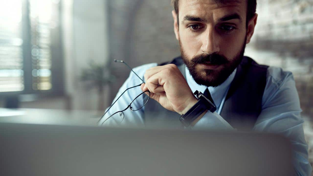 A man holding glasses while looking intently at a laptop screen.