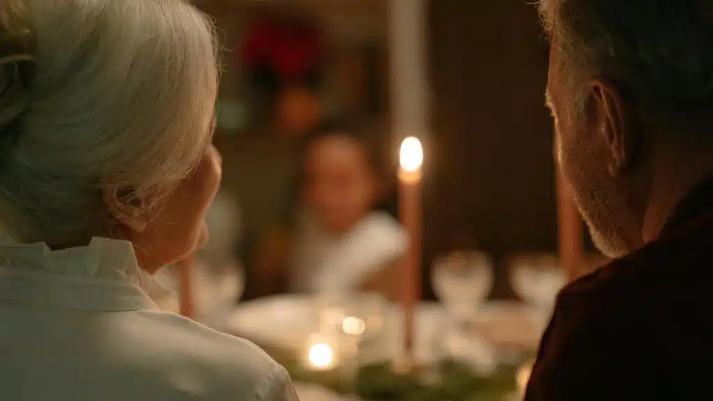 A couple sitting at a candlelit dinner table with blurred guests in the background.