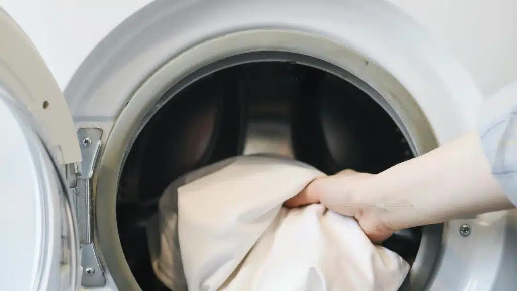 A person’s hand placing laundry into a washing machine.