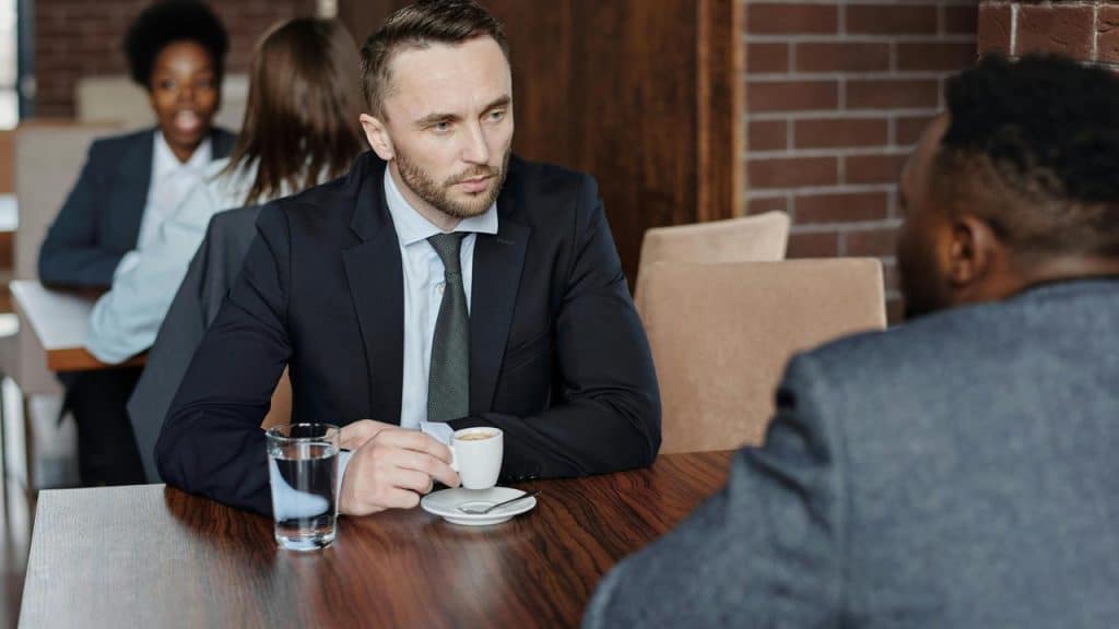 A man in a suit sitting at a café table having a serious conversation with another man.