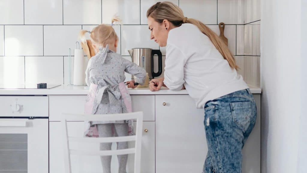 A woman helping a child at a kitchen counter.