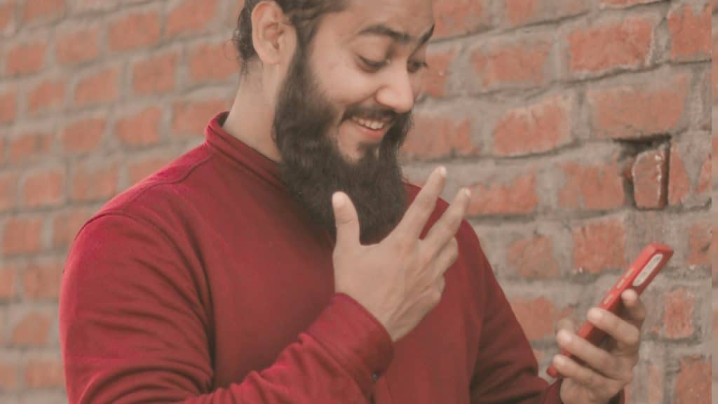 A man with a beard pointing using a cell phone.