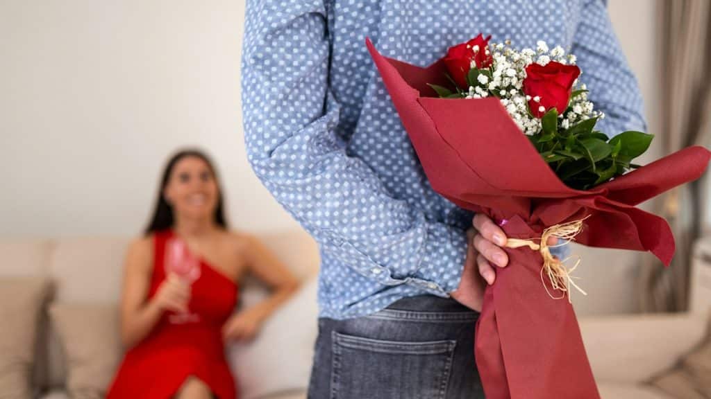 A man hiding a bouquet of roses behind his back to surprise his wife.