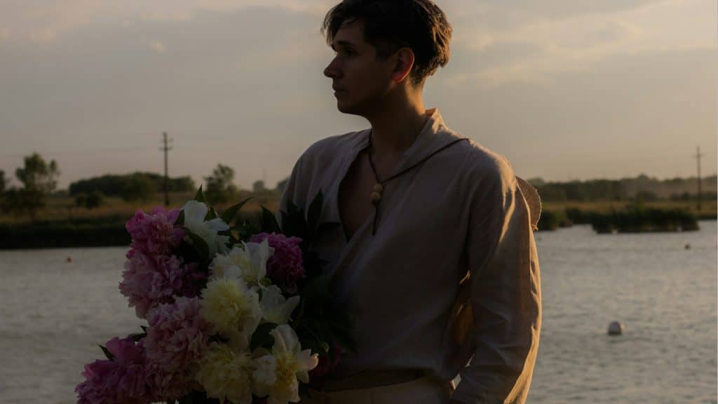 A man holding a bouquet of flowers by the water.